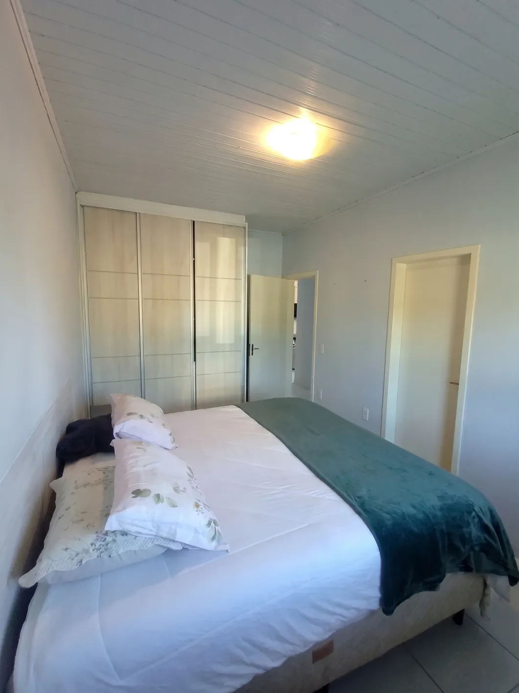 Dormitório de casal com guarda-roupa planejado de correr, cama e acesso ao corredor.