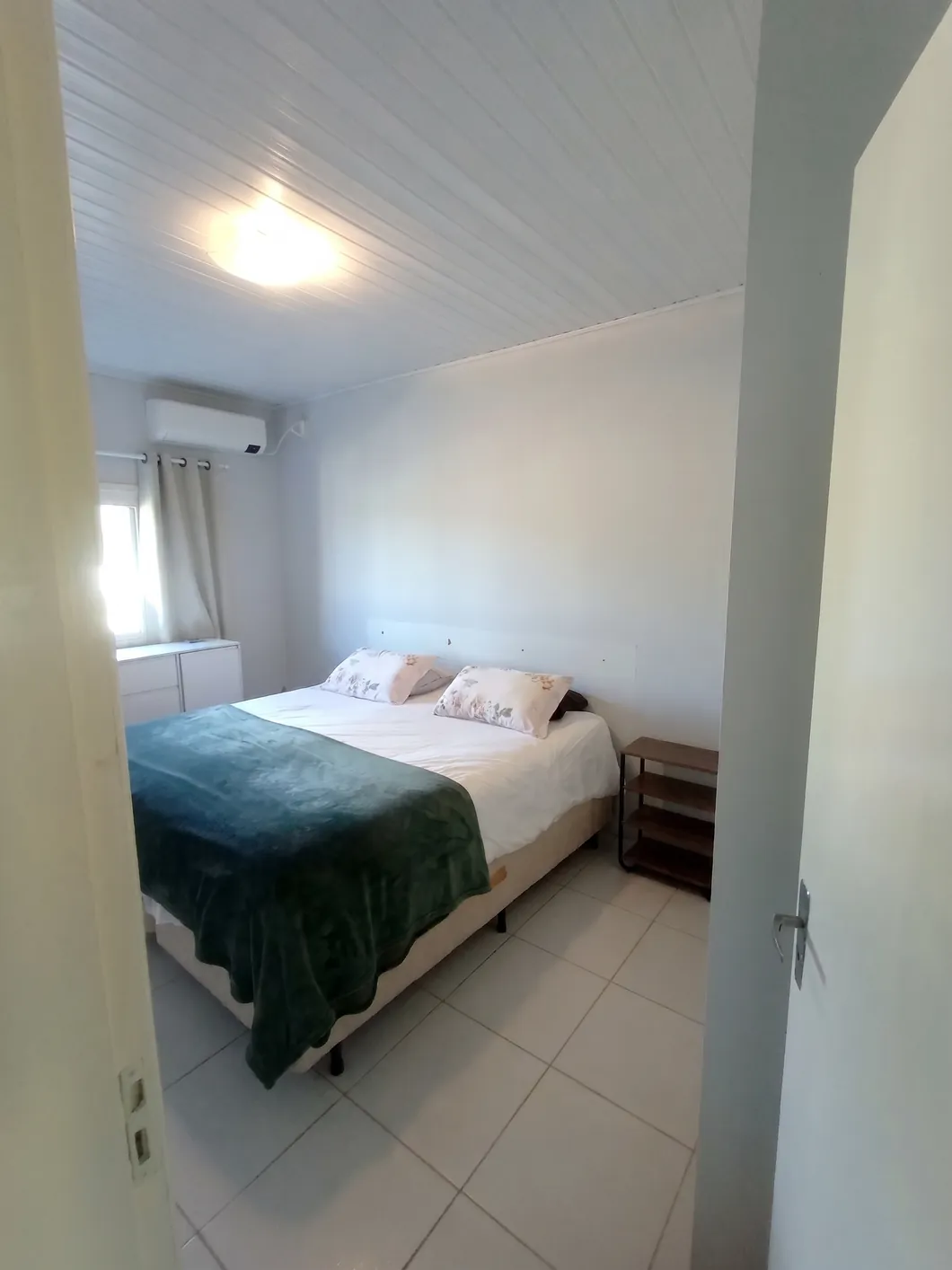 Segundo dormitório com cama de casal, cômoda e ar-condicionado na parede.