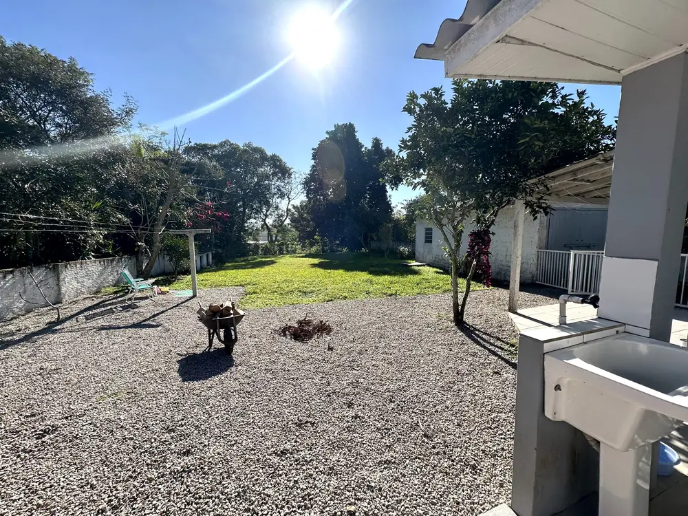 Pátio de pedrisco junto à casa, com gramado ao redor e vegetação alta ao fundo.