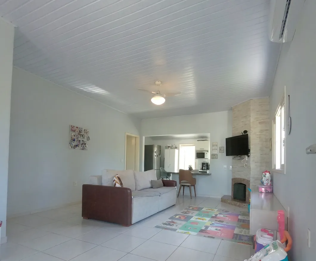 Sala de estar com piso branco, sofá, lareira de alvenaria à direita e passagem integrada para a cozinha ao fundo.