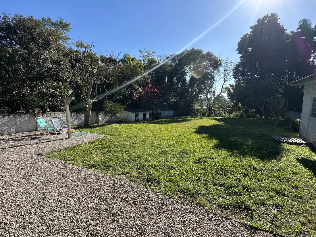 O terreno visto no comprimento: faixa longa de gramado que segue da casa até o fundo arborizado.